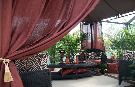 Outdoor maroon curtains in Dubai paired with black chairs and table, creating a stylish and cozy outdoor seating area.
